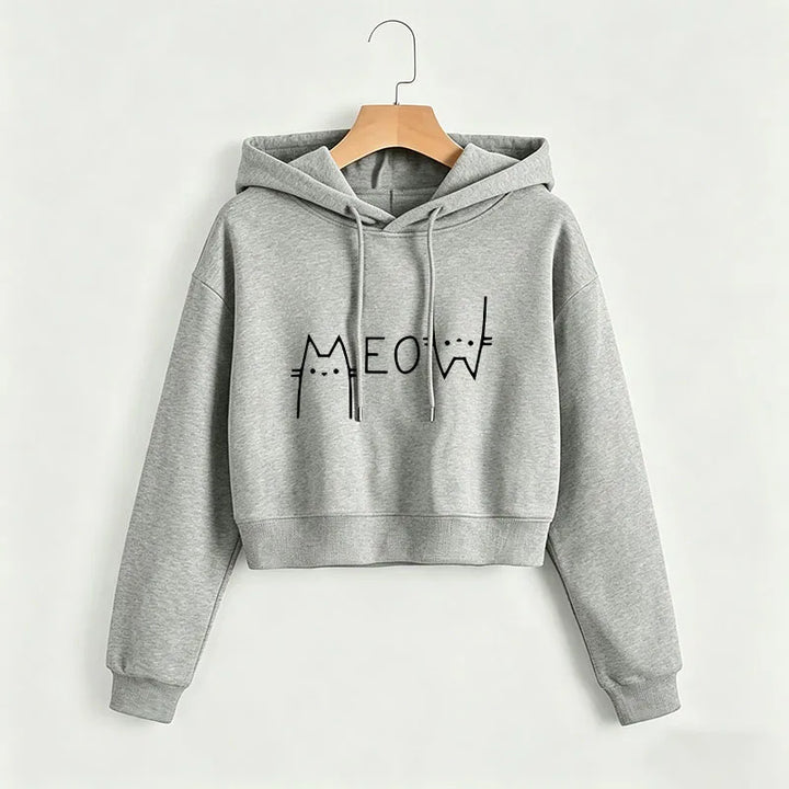 Heather gray cropped Meow hoodie on a wooden hanger against a light wall, showing a black cat print, hood and ribbed sleeves.