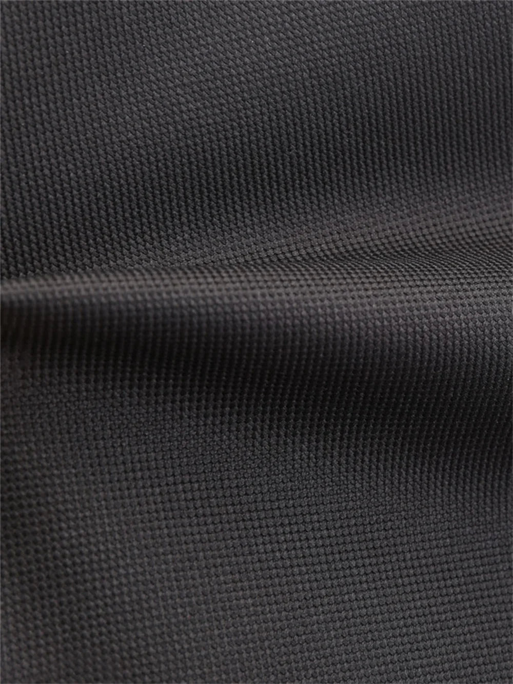 Close view of the black outer fabric on the backpack, with the woven surface texture and a stitched horizontal seam up close.