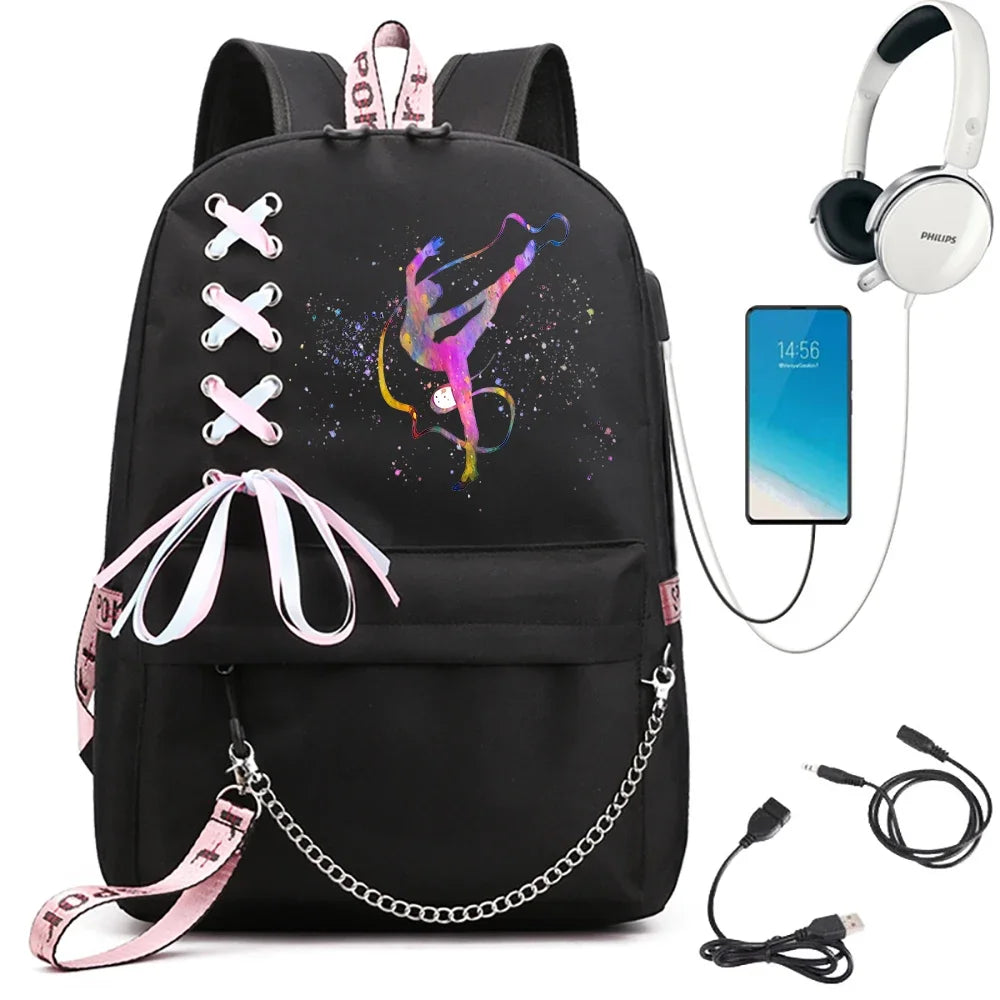 A black backpack featuring pink and purple ribbon gymnast artwork, light pink ribbon bow and chain, beside electronics props.