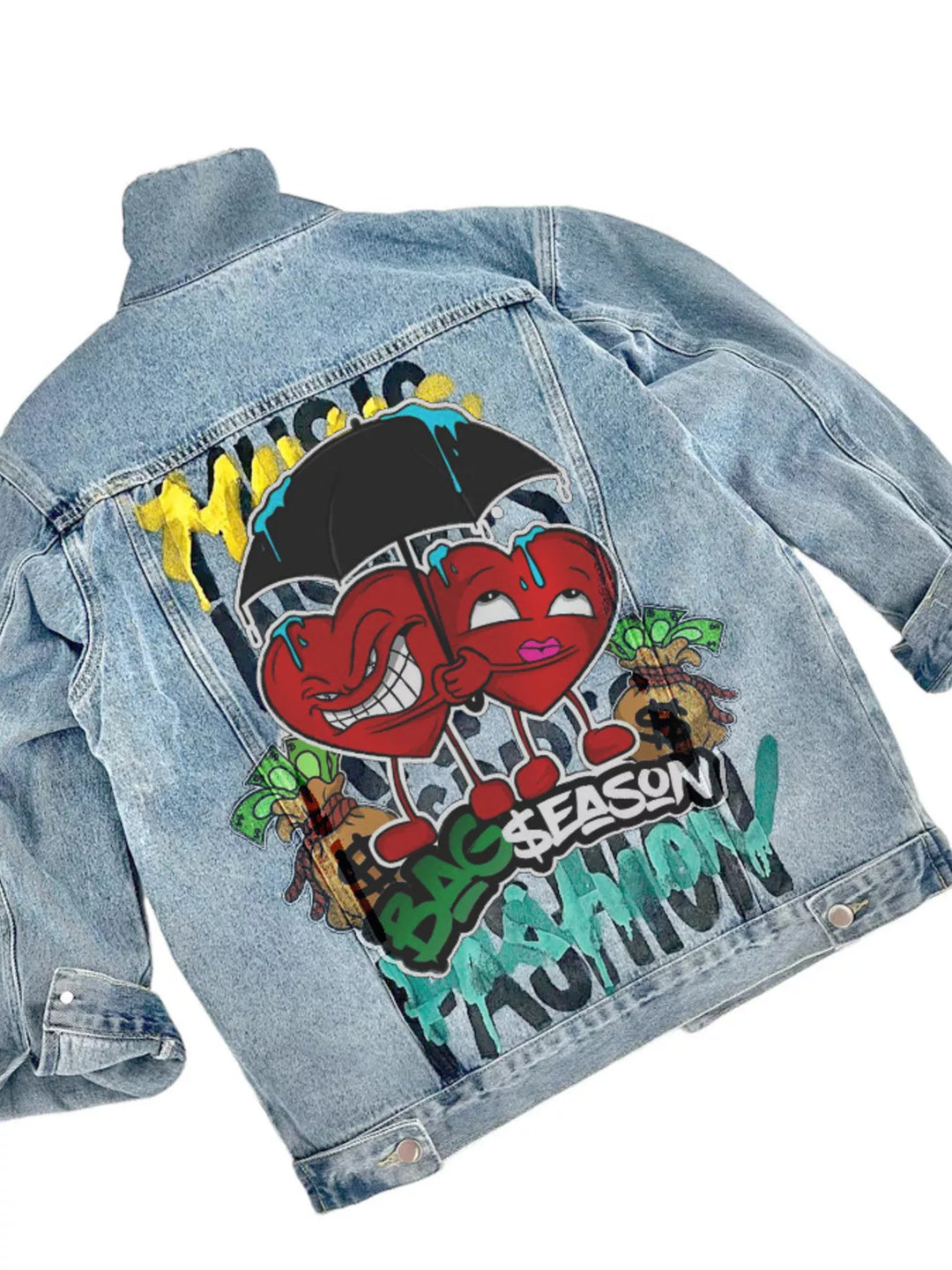 A light blue denim jacket shown from the back, featuring a large colorful graphic print with two cartoon hearts under a black umbrella, graffiti-style text, and small illustrated details.