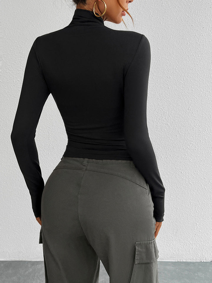 Person wearing a black long-sleeve top and gray cargo pants against a white wall.