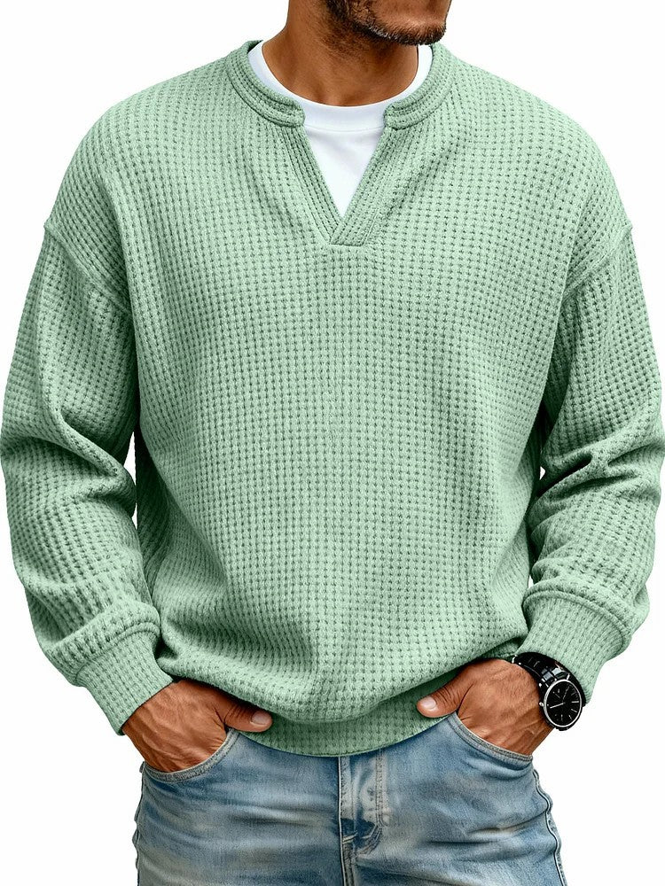 Person wearing a green textured sweater and blue jeans on a white background