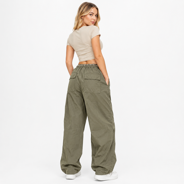 A woman shown from the back wearing wide-leg olive green cargo pants, a beige crop top, and white sneakers against a plain white studio background.