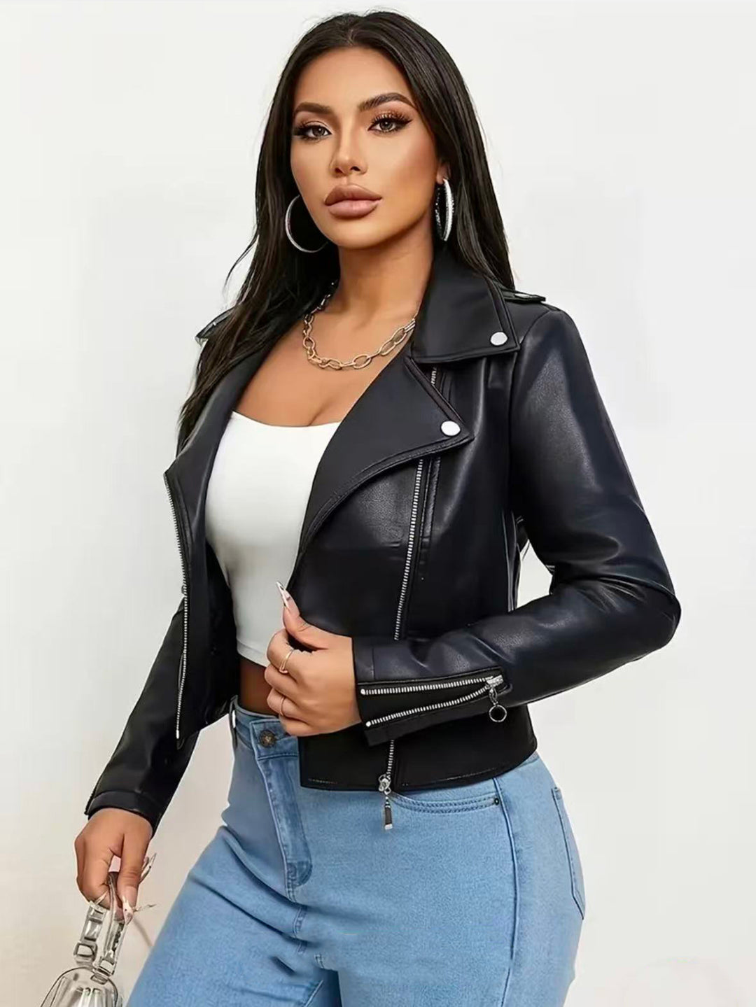 Black cropped moto jacket on a model in blue jeans, with wide lapels, silver snap buttons, long sleeves and cuff zip details.