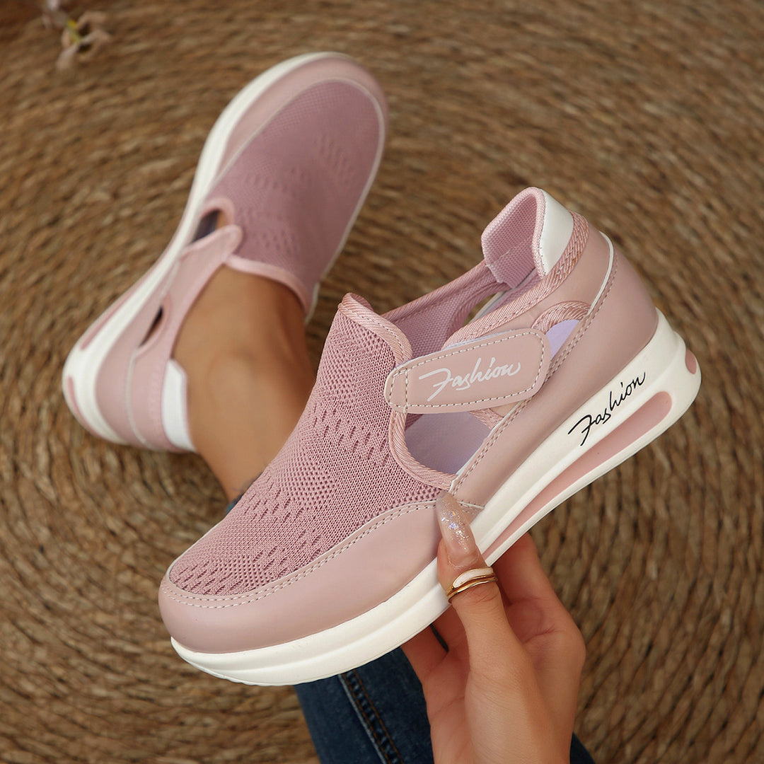 Pink slip-on shoes with white soles held by a hand on a textured brown surface