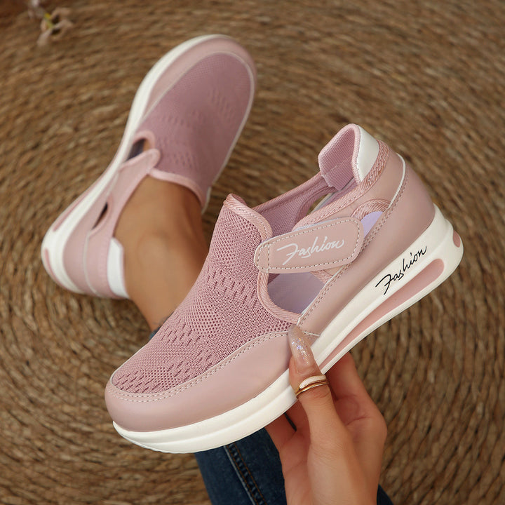 Pink slip-on shoes with white soles held by a hand on a textured brown surface