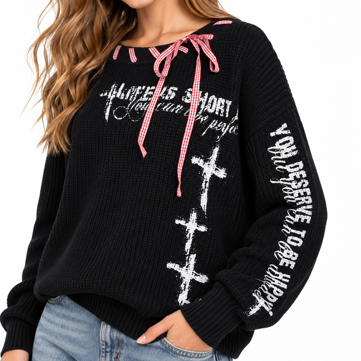 Black knit sweater detail showing white graphic print, sleeve text and gingham tie