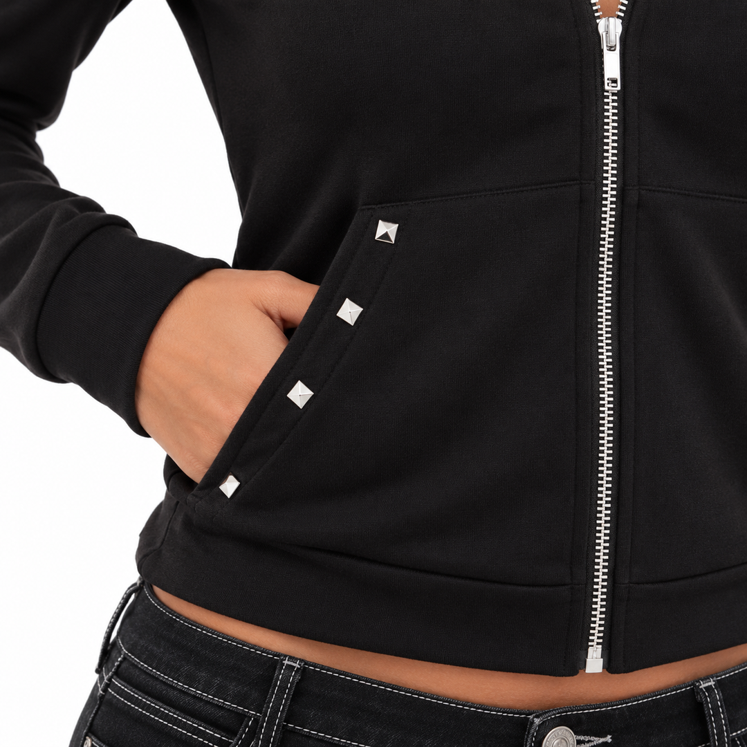 Close-up of the black hoodie pocket with silver pyramid studs, a hand inside the opening and an adjacent silver front zipper.