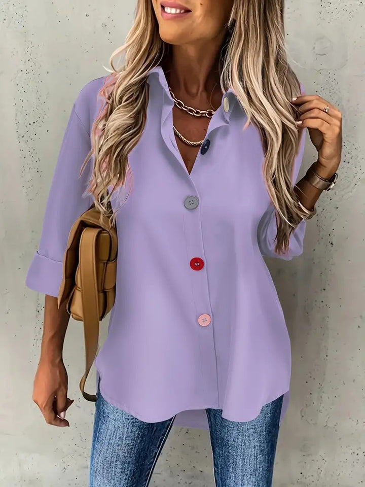Woman wearing a light purple button-up shirt and blue jeans against a plain background