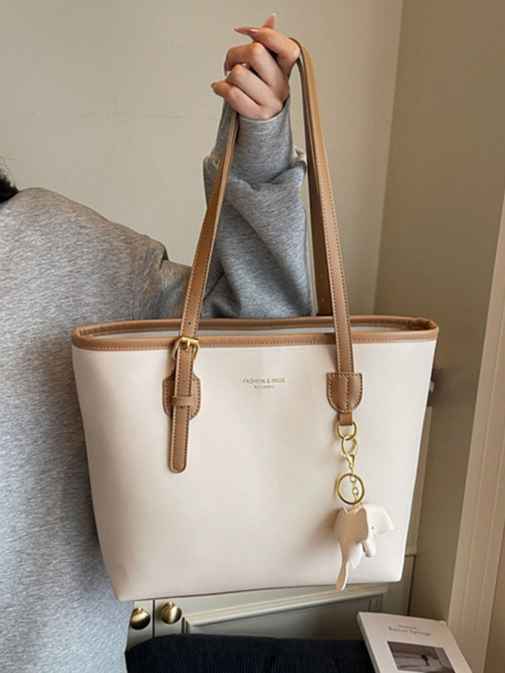 Person holding a beige handbag with brown straps and an elephant keychain.