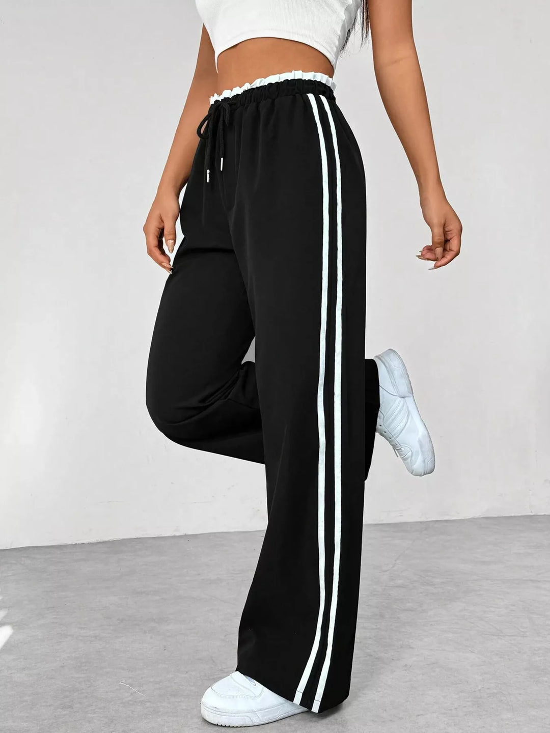 Black track pants with white stripes worn by a person on a plain background
