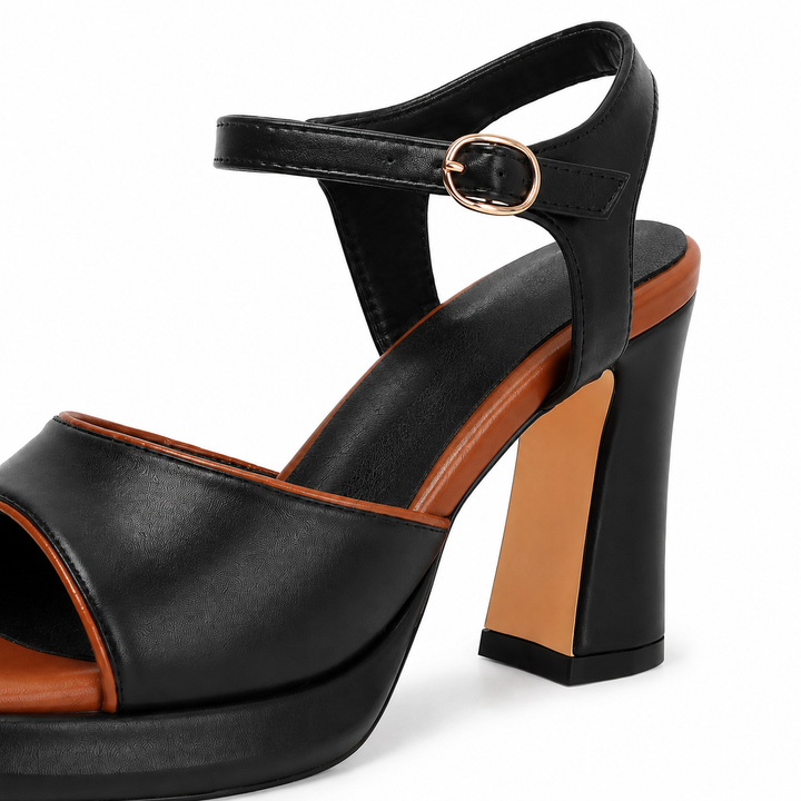 Close-up of black sandal ankle buckle, strap stitching and chunky heel with contrast insert on clean white studio background.