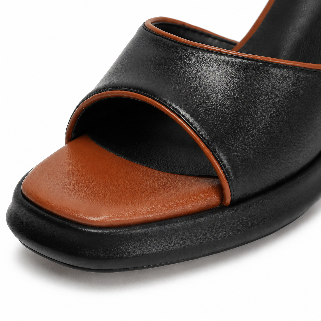 Macro view of black sandal front strap, stitching, textured surface, tan footbed and black platform sole on white studio.