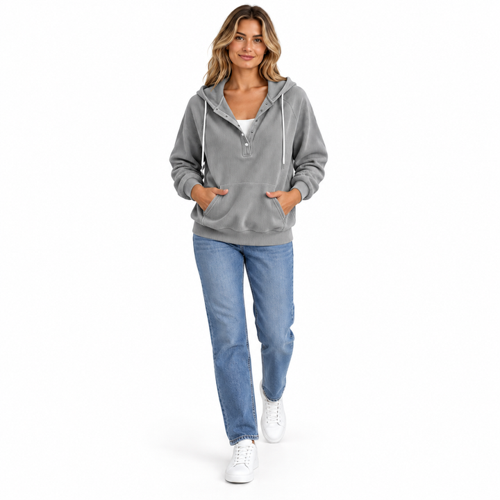 Adult woman wearing a grey hooded pullover with blue jeans and white sneakers, shown walking against white studio background.