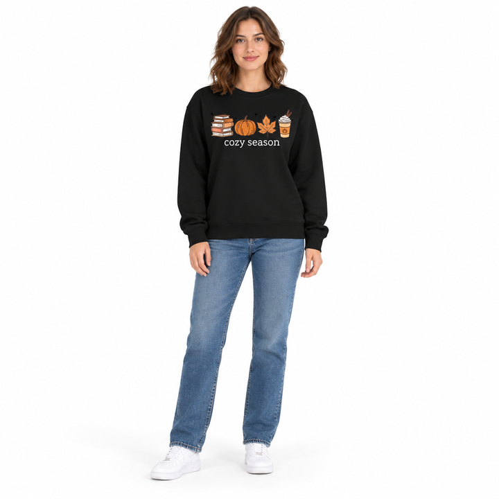 Black crewneck sweatshirt with white cozy season lettering and orange autumn artwork worn with blue jeans and white sneakers.