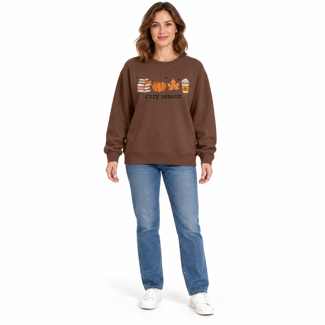 Coffee brown sweatshirt worn by a full-length model in blue jeans, showing books, a pumpkin, leaf and latte across the chest.