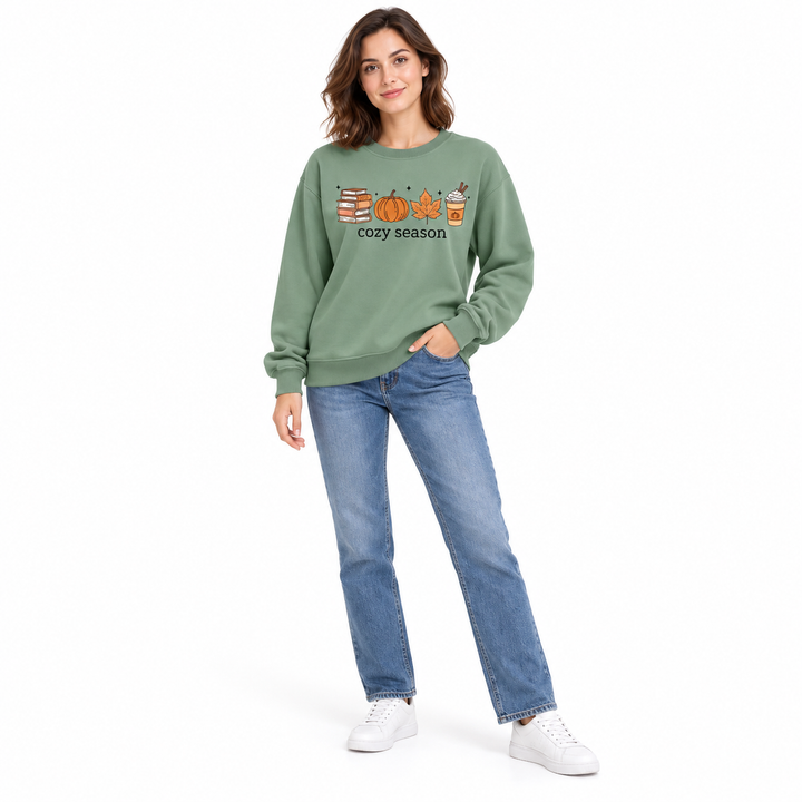Olive green sweatshirt on a woman in blue jeans, showing the front autumn graphic and loose sleeves against white background.