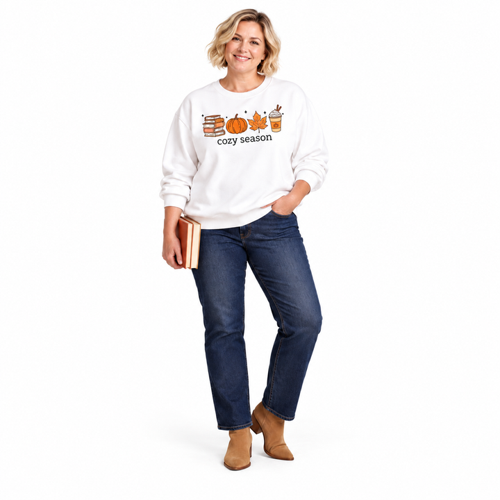 A white cozy season sweatshirt on a blonde woman wearing dark jeans and ankle boots, holding books against a white background