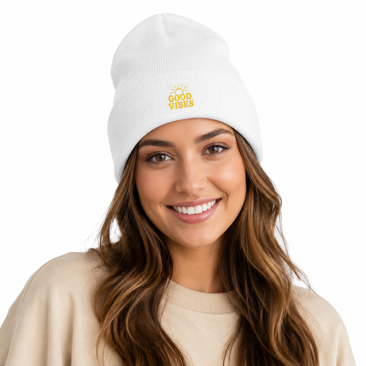 Woman wearing white cuffed beanie with embroidered Good Vibes design, smiling in a clean white studio portrait