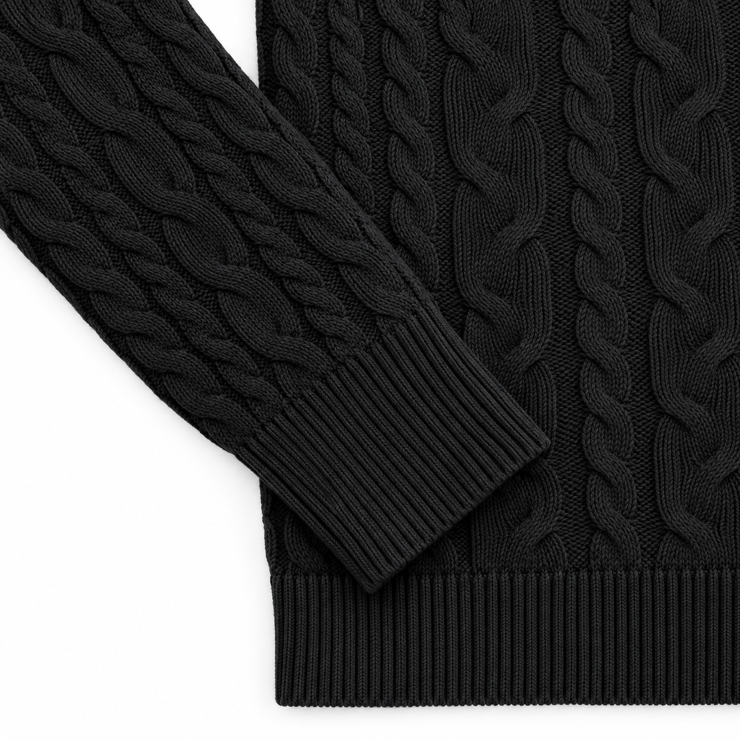 Black sweater detail showing the cable knit sleeve, ribbed cuff and bottom hem, arranged on a bright white studio background.