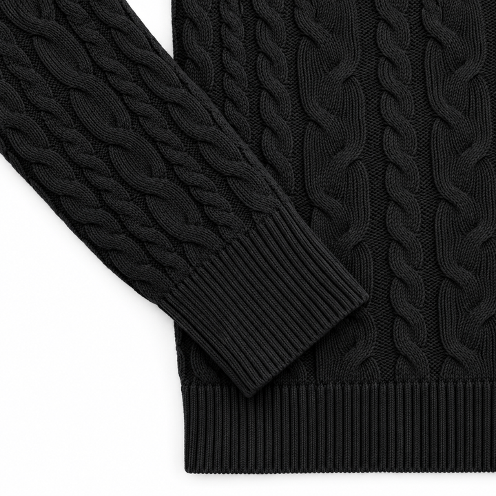 Black sweater detail showing the cable knit sleeve, ribbed cuff and bottom hem, arranged on a bright white studio background.