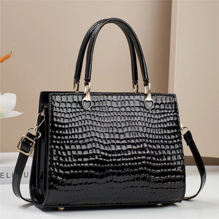 Black crocodile-patterned handbag on a light surface with a neutral background