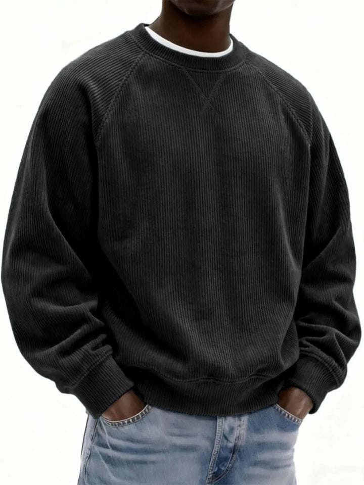 Person wearing a black corduroy sweatshirt and light blue jeans on a white background