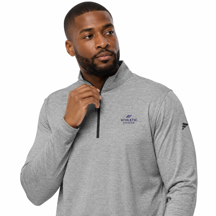 A man wearing a heather gray quarter-zip pullover sweatshirt with a dark blue &