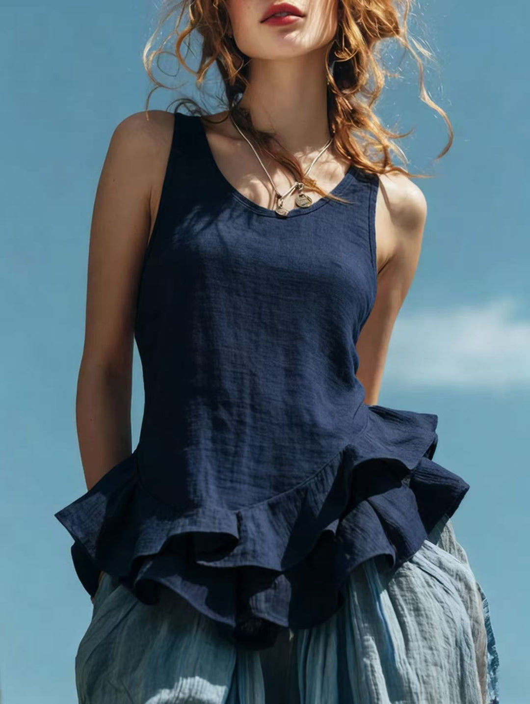 Woman wearing a navy blue ruffled top against a clear blue sky