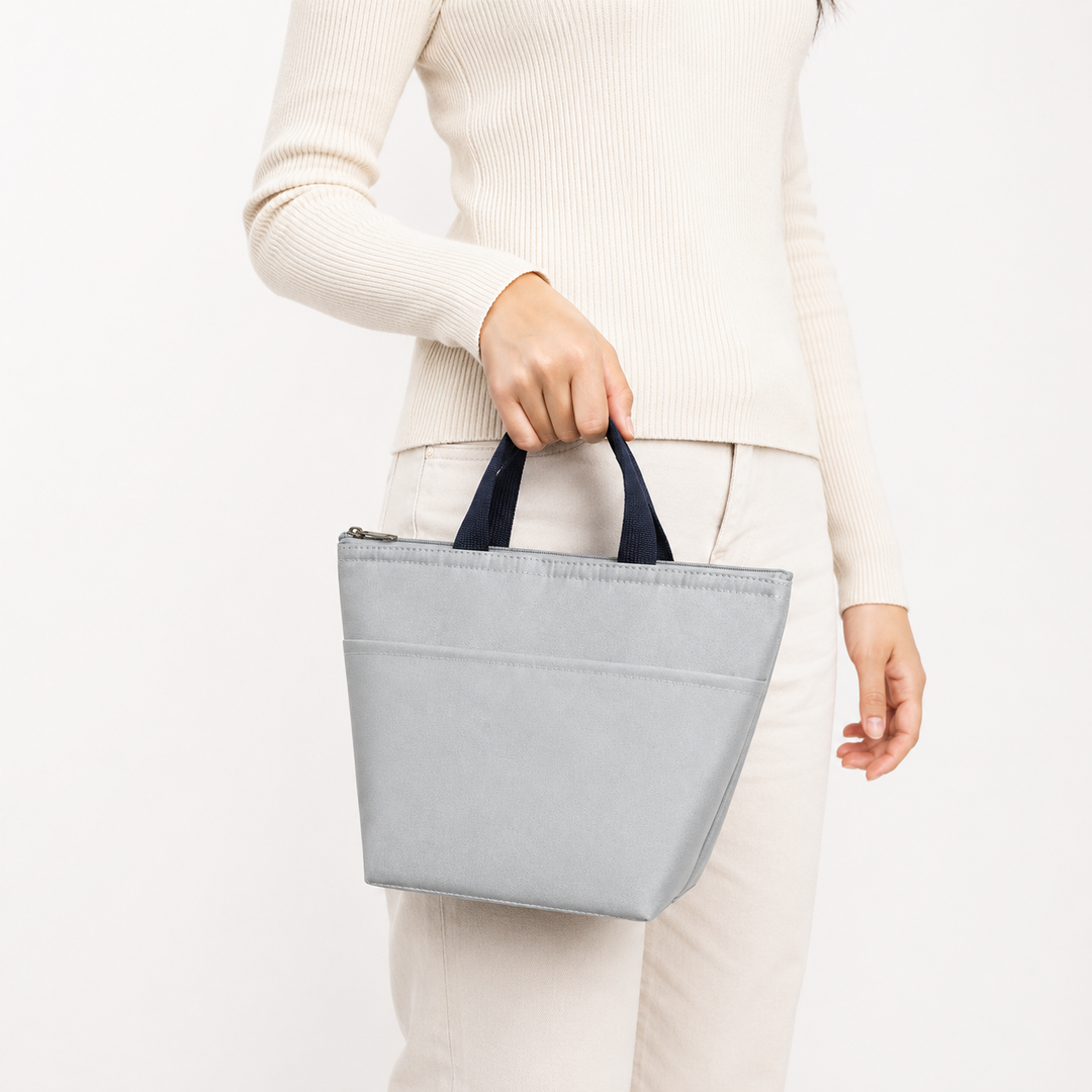 Light gray portable lunch tote carried by a woman, showing compact proportions, short navy handles and simple everyday shape.