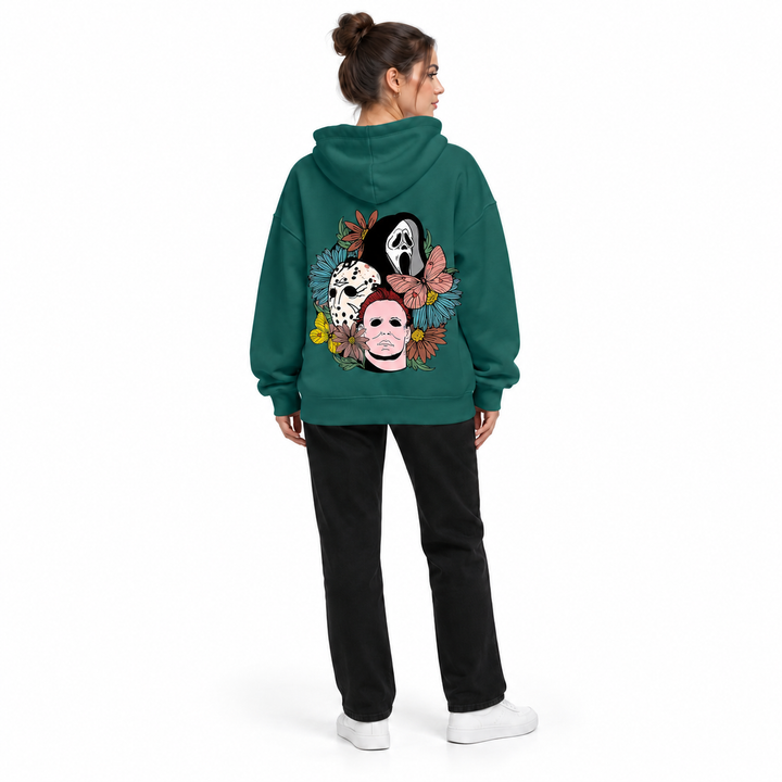 Full-body rear view of a woman wearing the dark green hoodie with a mask and flower print, black trousers and white sneakers.