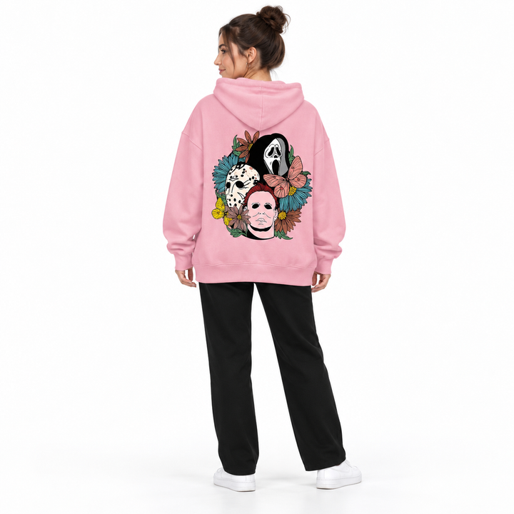 Full-body rear view of a woman wearing the pink hooded pullover with a mask and flower print, black trousers and white shoes.
