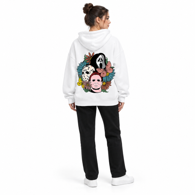 Full-body rear view of a woman wearing the white hooded pullover with floral mask back print, black trousers and white shoes.