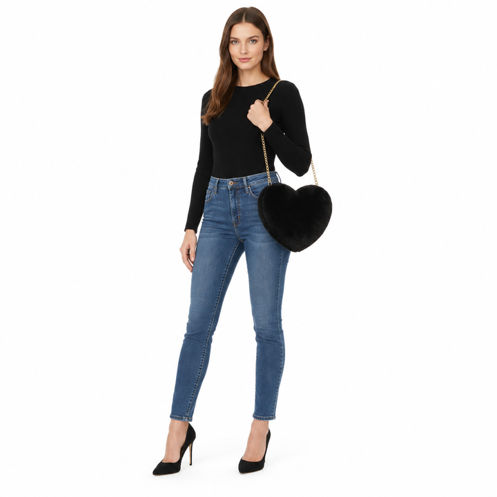 Full-body brunette woman carrying a black plush heart bag with a chain strap, styled with a black top and jeans in the studio