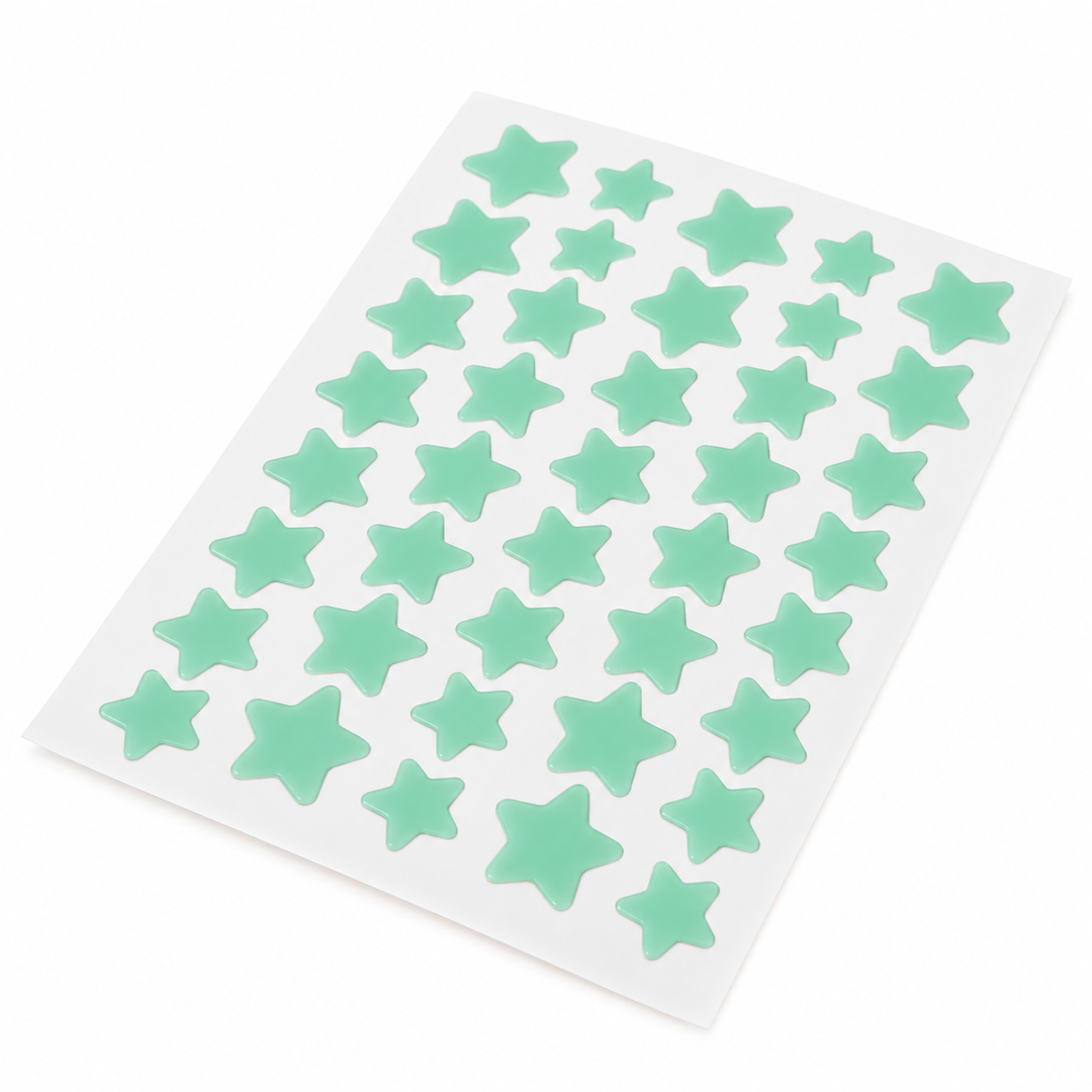 Angled view of a mint green sheet of star-shaped patches showing the alternating star sizes against a white photo background.