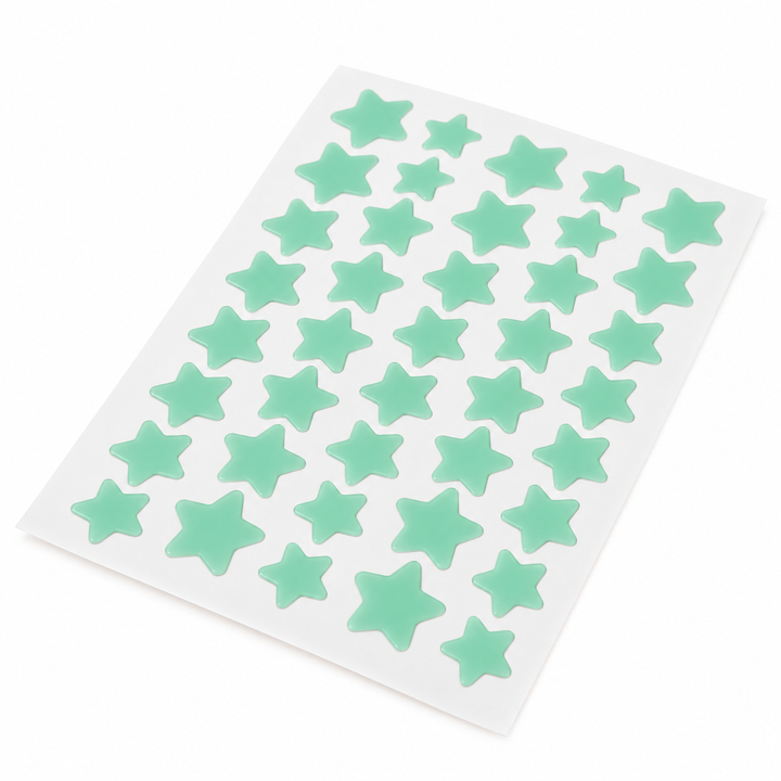 Angled view of a mint green sheet of star-shaped patches showing the alternating star sizes against a white photo background.