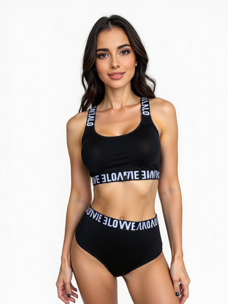 A woman modeling a black two-piece bikini set with white text on the straps and waistbands, photographed against a plain white studio background.