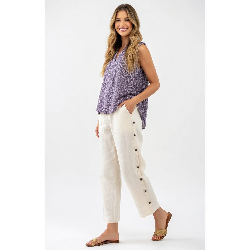 Woman wearing a purple sleeveless top and white pants with buttons on a white background