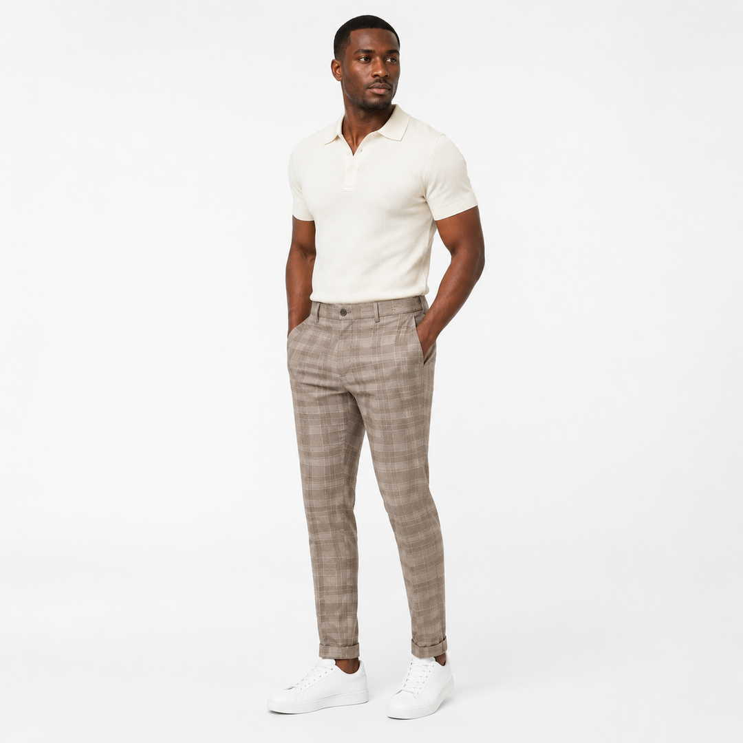 Khaki plaid trousers on an adult Black male model in a three-quarter studio view with a cream polo and simple white sneakers.