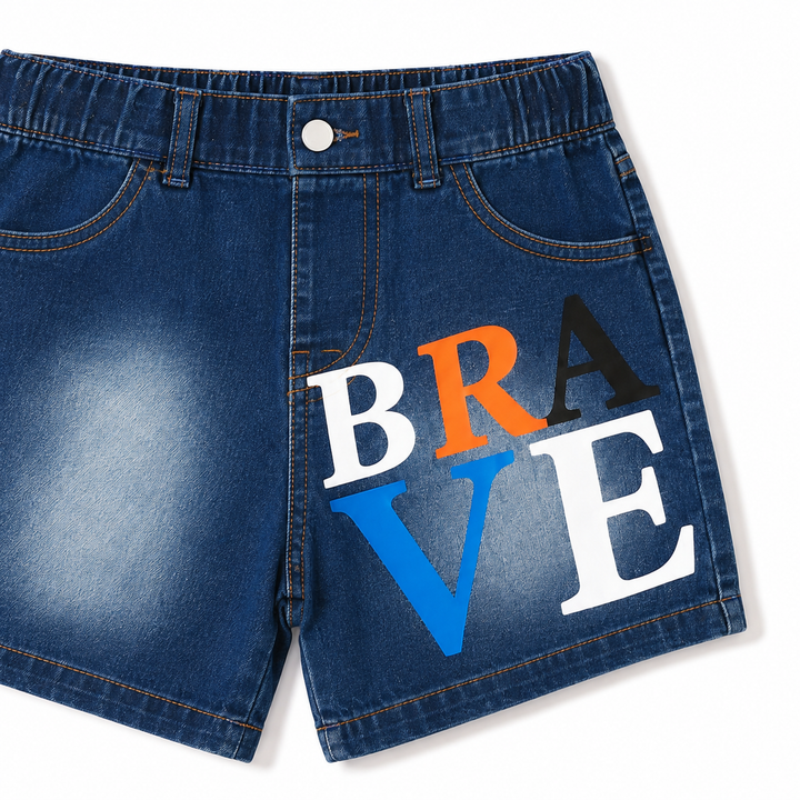 Close-up of denim shorts with large BRAVE letter graphic, washed finish, seams and front construction on white background.