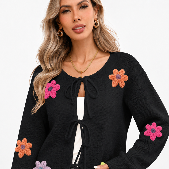 Black floral tie-front knit cardigan close view on a woman, showing knit texture, colorful flower appliques and bow closures.