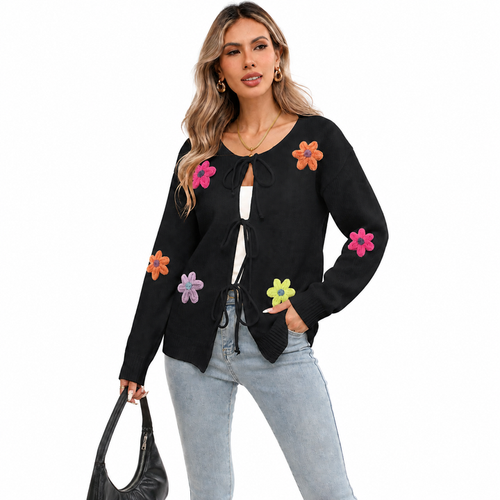 Black floral tie-front knit cardigan on a woman with visible face, light-wash jeans, flower appliques and black handbag.