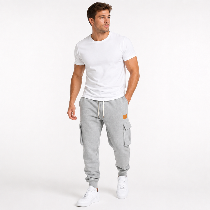 Male model wearing light gray cargo jogger pants in a natural movement pose on a white studio background.