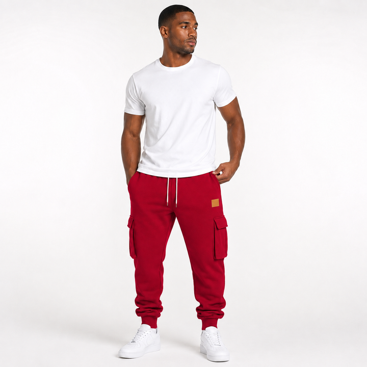 Male model wearing red cargo jogger pants with cargo pockets and drawstring waist clearly visible on a white studio background.
