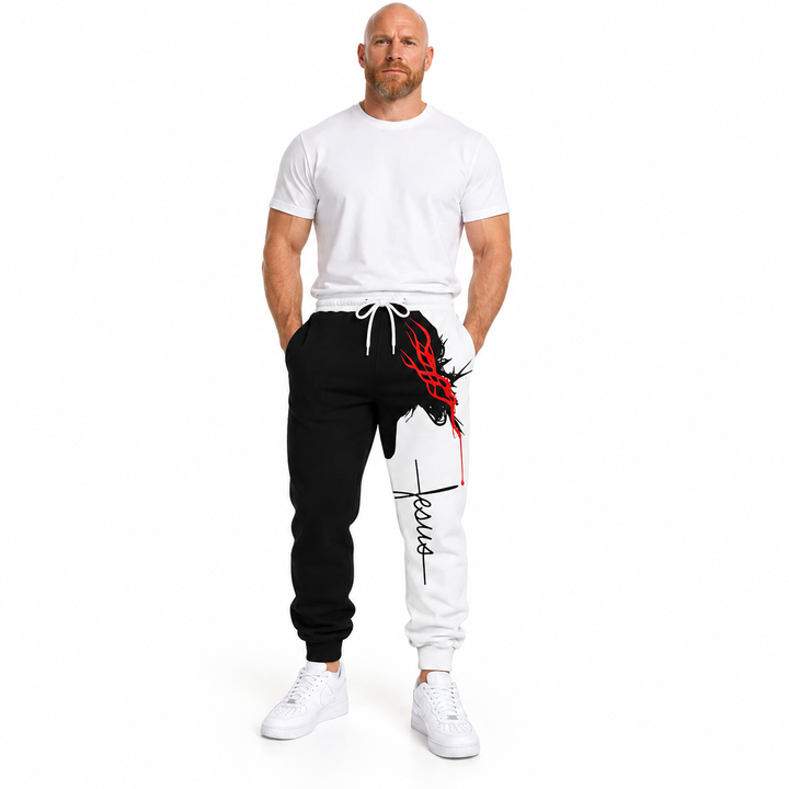 Bald male model with a ginger beard wearing black and white Jesus print pants, a plain white tee and white sneakers in studio