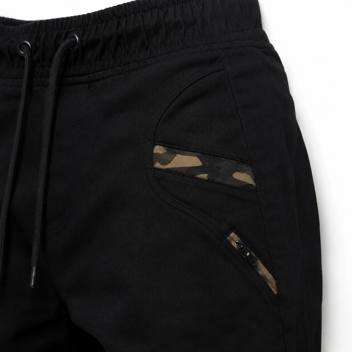Black jogger pants close-up showing camouflage pocket trim, zipper detail, stitching and cotton blend fabric texture fit view