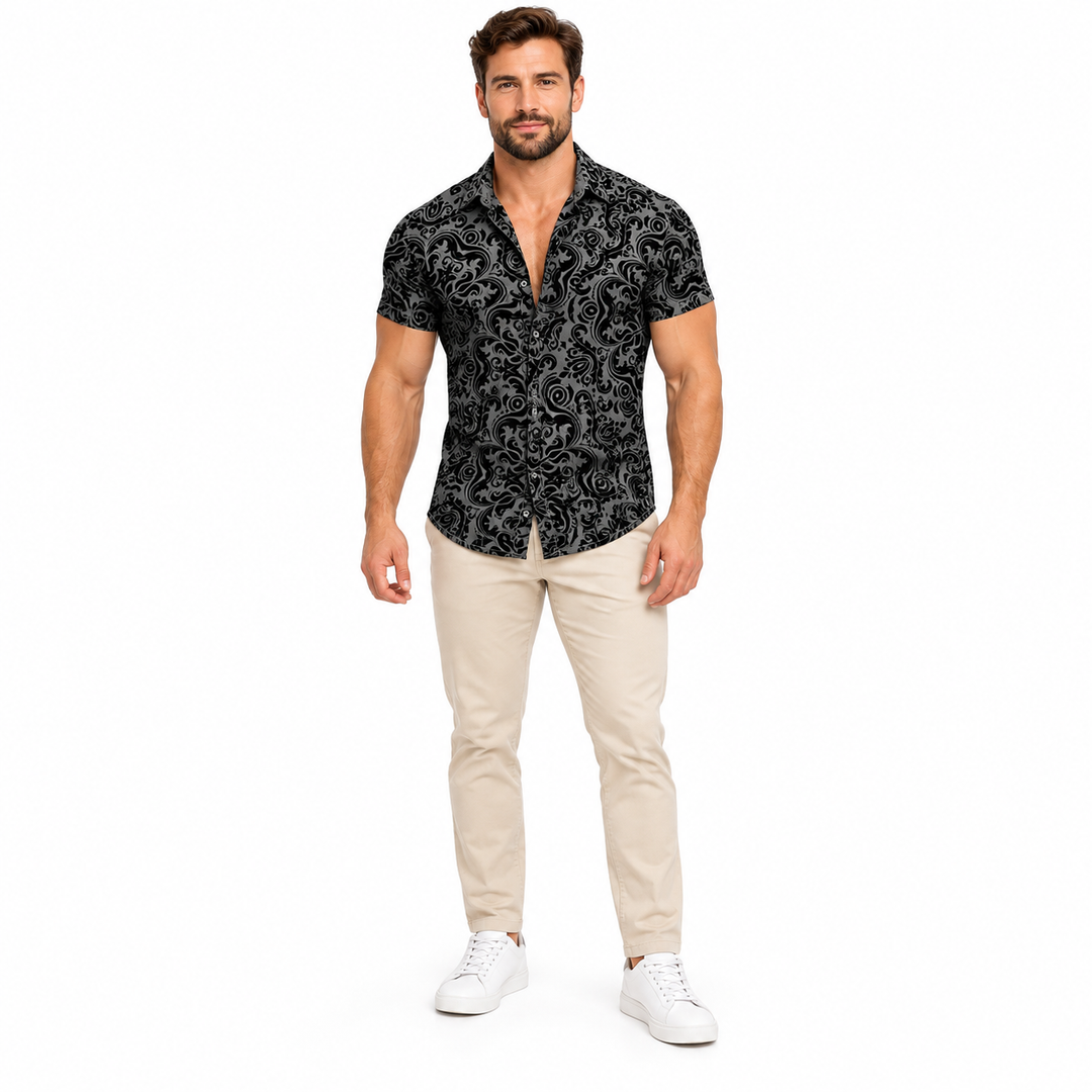 Male model shown wearing the black and grey scroll print collared shirt with beige trousers and white sneakers against white.