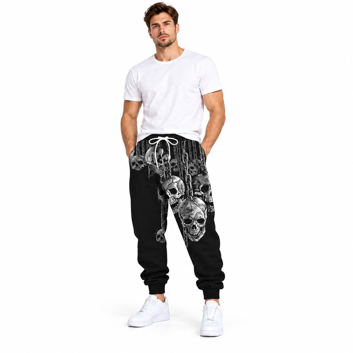 Male model wearing gray skull pattern printed pants, with a plain white tee and white sneakers, on a white studio background.