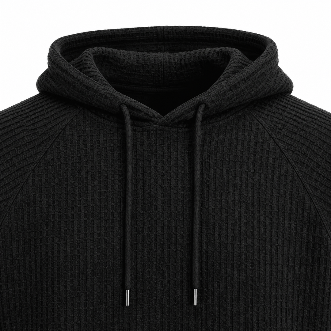 Black waffle knit hoodie close-up showing hood, drawstrings and raglan seam construction.