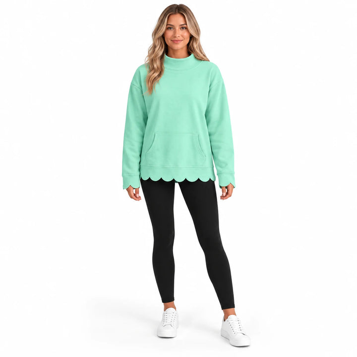 Full-body model wearing a mint green pullover with a mock collar, front pocket and scalloped edges with leggings and sneakers